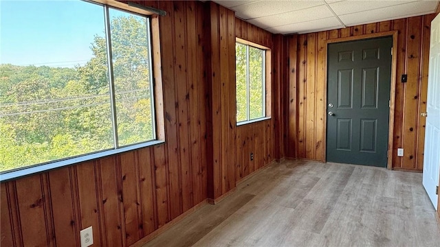 entrance foyer with wooden walls, a paneled ceiling, and light wood-style floors