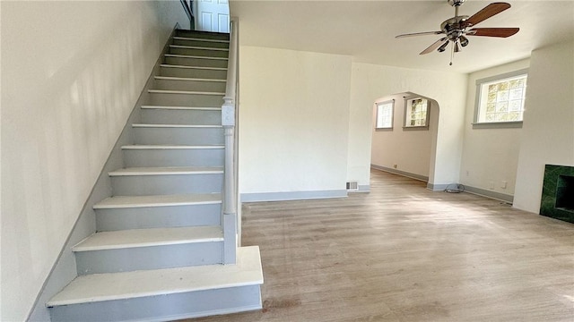 stairs featuring wood finished floors, a ceiling fan, baseboards, a fireplace, and arched walkways