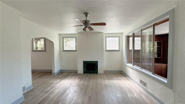 unfurnished living room featuring a fireplace, wood finished floors, visible vents, and ceiling fan