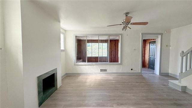 unfurnished living room with wood finished floors, visible vents, a fireplace, ceiling fan, and stairs