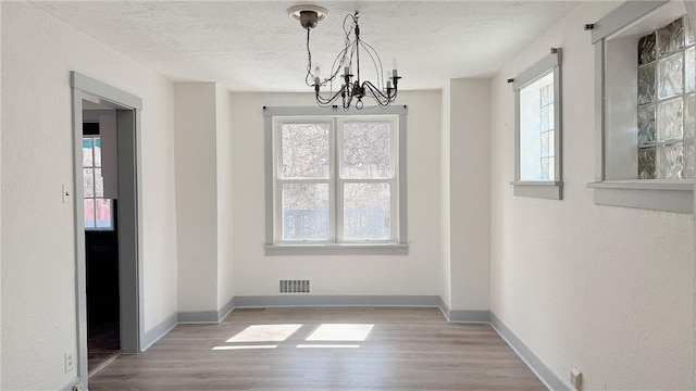 unfurnished dining area with a notable chandelier, a textured ceiling, light wood-type flooring, and visible vents