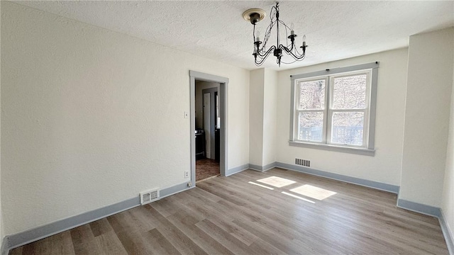 unfurnished dining area featuring a notable chandelier, wood finished floors, visible vents, and a textured ceiling