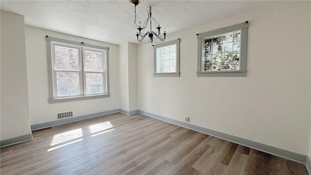 unfurnished dining area with visible vents, baseboards, a chandelier, wood finished floors, and a textured ceiling