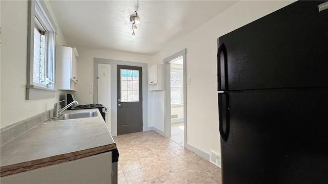 kitchen featuring visible vents, light countertops, freestanding refrigerator, white cabinets, and a sink