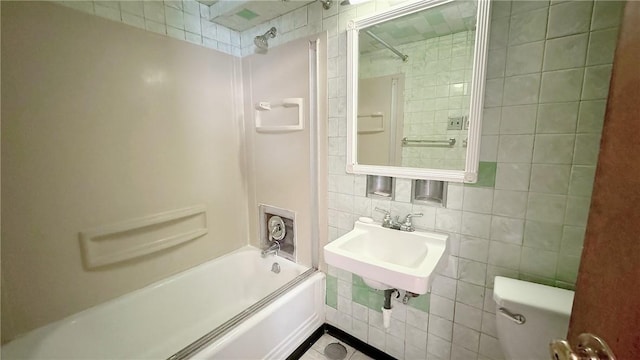 bathroom with tub / shower combination, toilet, tile walls, and a sink