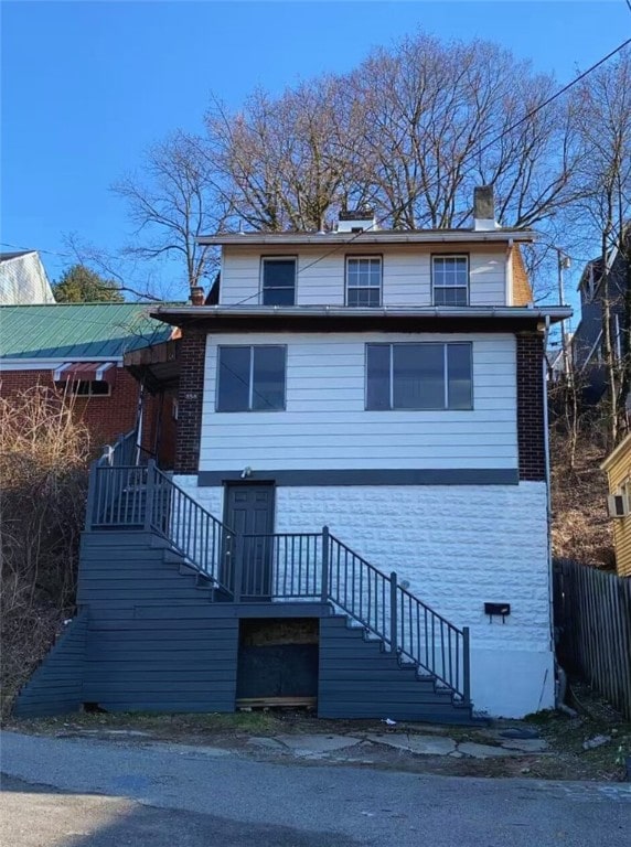 view of front of home featuring brick siding, a chimney, stairs, and fence