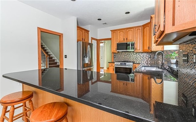 kitchen with dark stone counters, tasteful backsplash, sink, kitchen peninsula, and appliances with stainless steel finishes