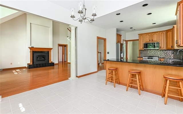 kitchen featuring appliances with stainless steel finishes, light hardwood / wood-style floors, kitchen peninsula, a tiled fireplace, and a notable chandelier