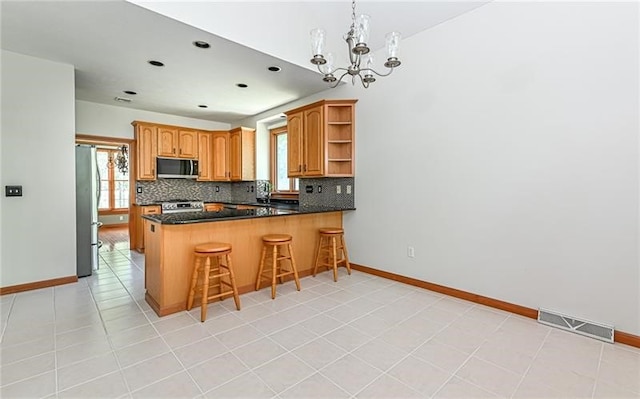 kitchen featuring hanging light fixtures, kitchen peninsula, stainless steel appliances, a kitchen bar, and an inviting chandelier