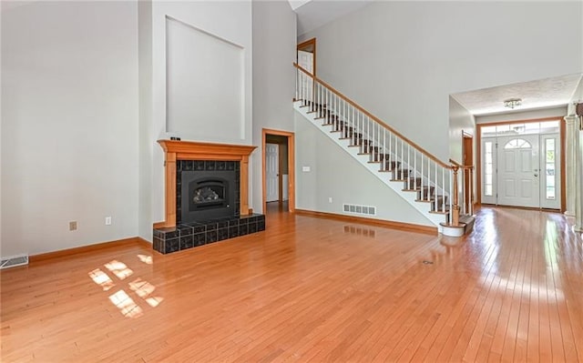 unfurnished living room with wood-type flooring, a towering ceiling, and a tiled fireplace