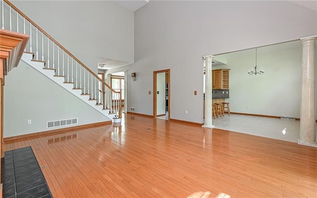 unfurnished living room featuring wood-type flooring, a notable chandelier, a towering ceiling, and decorative columns