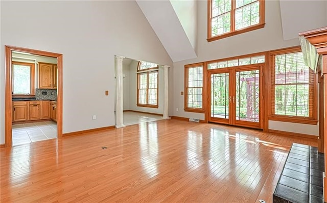 unfurnished living room featuring light wood-type flooring, decorative columns, and a high ceiling