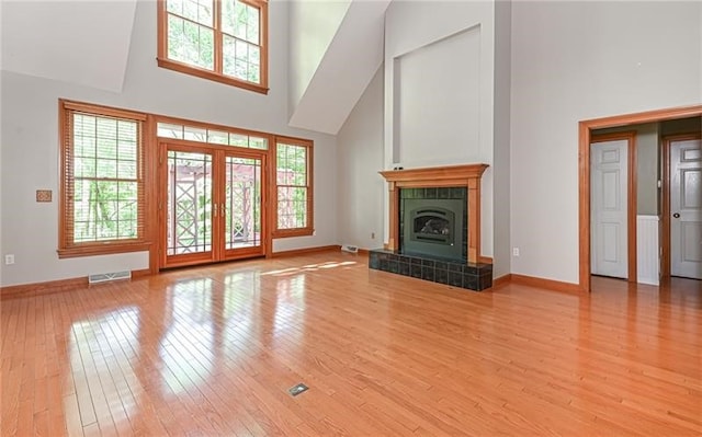 unfurnished living room with a towering ceiling, a tiled fireplace, hardwood / wood-style flooring, and a healthy amount of sunlight