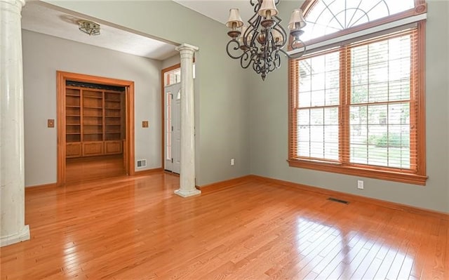 spare room featuring an inviting chandelier, light hardwood / wood-style floors, decorative columns, and a healthy amount of sunlight