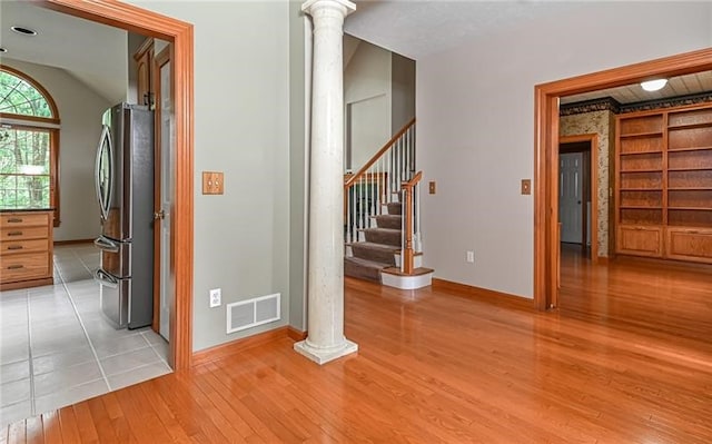 hall with light hardwood / wood-style flooring, ornate columns, and lofted ceiling