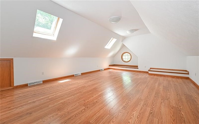 bonus room with light wood-type flooring, a healthy amount of sunlight, and vaulted ceiling with skylight