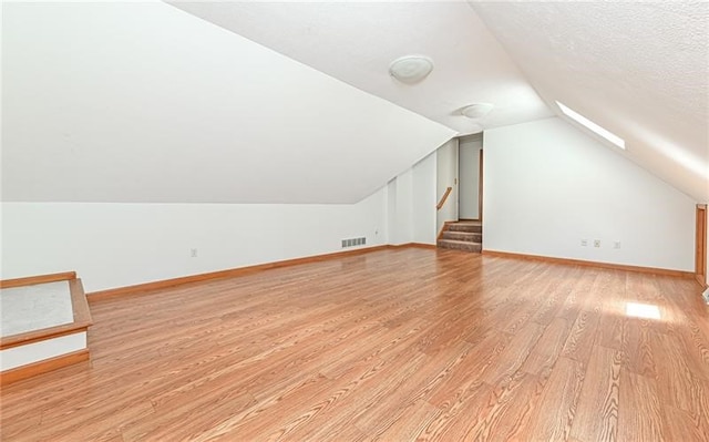 additional living space featuring a textured ceiling, vaulted ceiling with skylight, and light hardwood / wood-style flooring