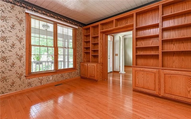 empty room featuring light hardwood / wood-style flooring, built in features, and decorative columns