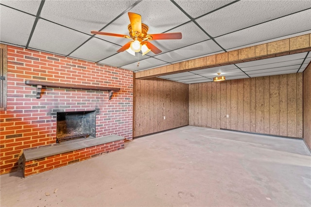 unfurnished living room with ceiling fan, wooden walls, concrete flooring, and a fireplace