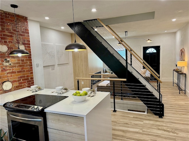 kitchen with pendant lighting, stainless steel electric stove, brick wall, and light hardwood / wood-style flooring