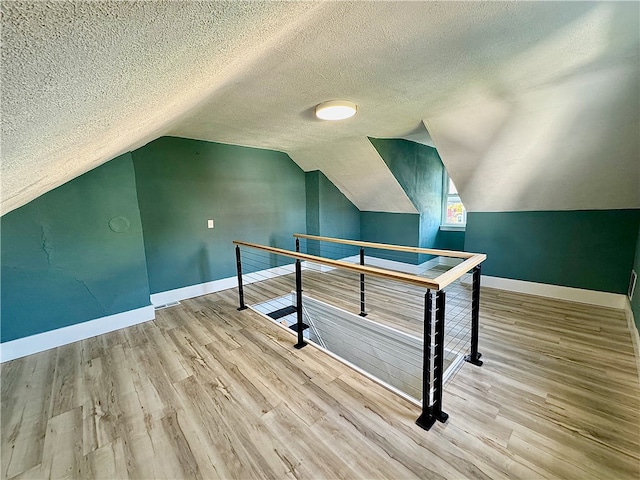 additional living space featuring vaulted ceiling, a textured ceiling, and light hardwood / wood-style flooring