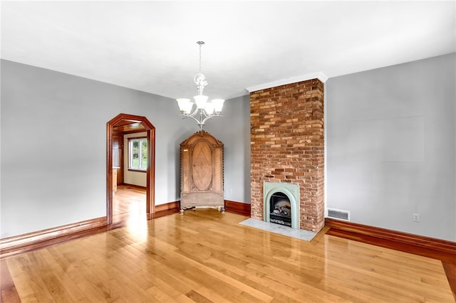 unfurnished living room featuring wood-type flooring, a brick fireplace, and an inviting chandelier