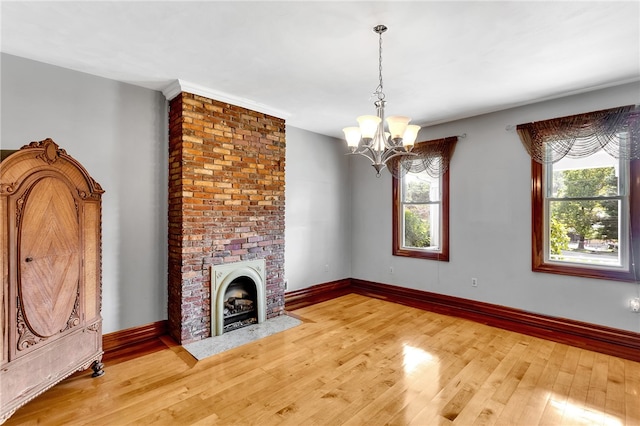 unfurnished living room featuring hardwood / wood-style flooring, an inviting chandelier, and a brick fireplace