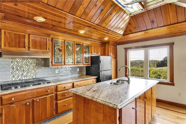 kitchen with stainless steel gas stovetop, light wood-type flooring, sink, black fridge, and a center island with sink