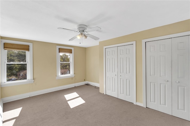 unfurnished bedroom with carpet flooring, ceiling fan, and multiple closets