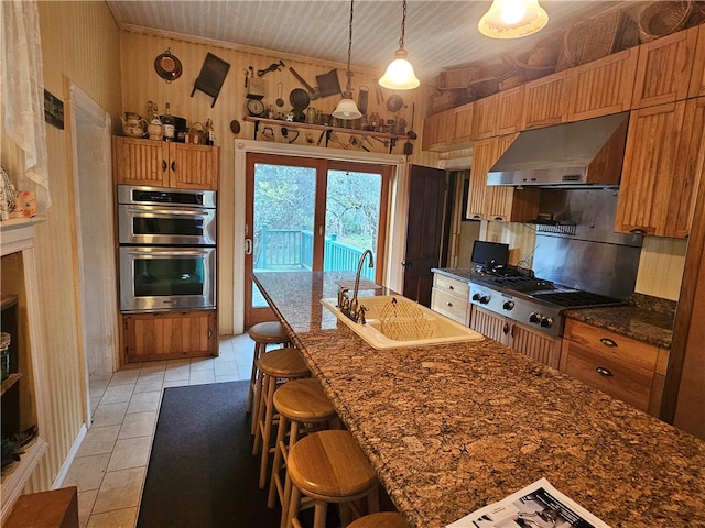 kitchen with hanging light fixtures, stainless steel appliances, sink, exhaust hood, and a breakfast bar