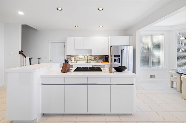 kitchen with light tile patterned floors, backsplash, high end refrigerator, sink, and white cabinets