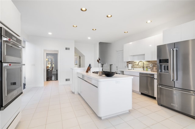 kitchen featuring backsplash, a center island, stainless steel appliances, sink, and white cabinetry