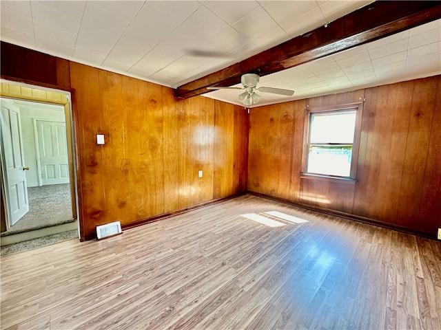 unfurnished room with ceiling fan, wood walls, beam ceiling, and light hardwood / wood-style floors