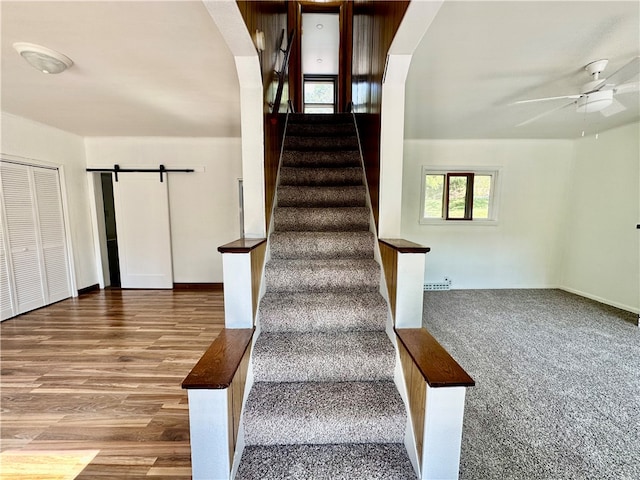 stairway featuring a barn door, hardwood / wood-style floors, and ceiling fan