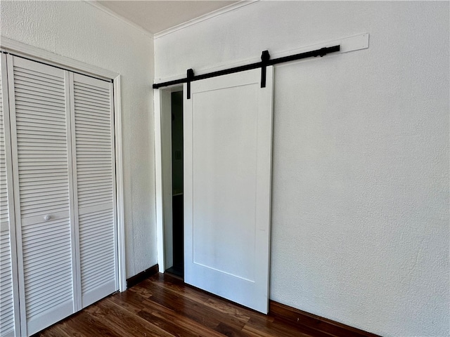 unfurnished bedroom with a barn door, a closet, and dark wood-type flooring