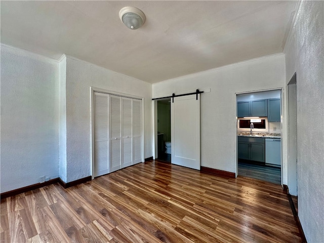 unfurnished bedroom featuring ensuite bathroom, a barn door, sink, a closet, and dark hardwood / wood-style floors