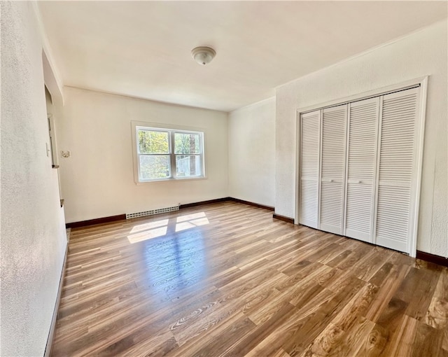 unfurnished bedroom with hardwood / wood-style flooring, a baseboard radiator, and a closet