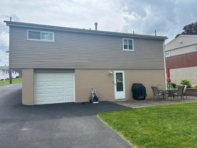 rear view of property featuring a lawn, a garage, and a patio