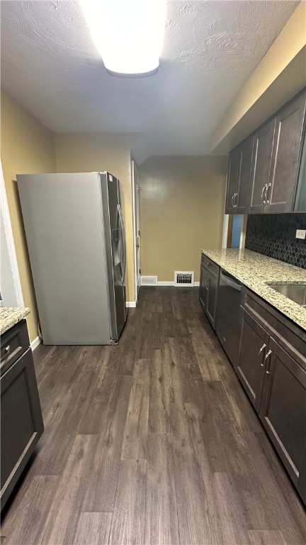 kitchen with sink, light stone counters, dark hardwood / wood-style flooring, stainless steel fridge, and dark brown cabinets