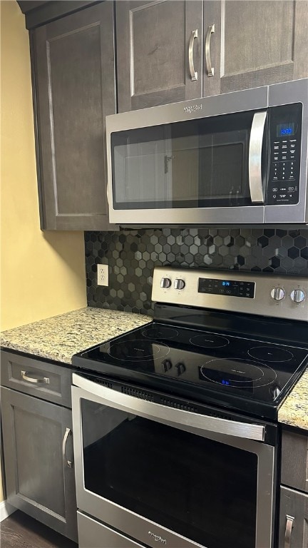 kitchen with tasteful backsplash, light stone countertops, dark hardwood / wood-style flooring, and appliances with stainless steel finishes