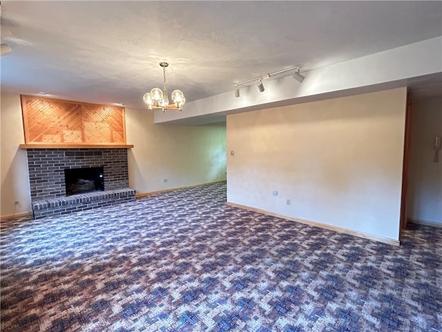 unfurnished living room featuring a brick fireplace, rail lighting, a chandelier, and dark carpet