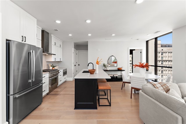 kitchen featuring a kitchen breakfast bar, light hardwood / wood-style flooring, appliances with stainless steel finishes, an island with sink, and white cabinets