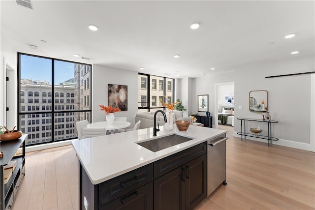 kitchen featuring dark brown cabinets, a center island with sink, light hardwood / wood-style flooring, stainless steel dishwasher, and sink