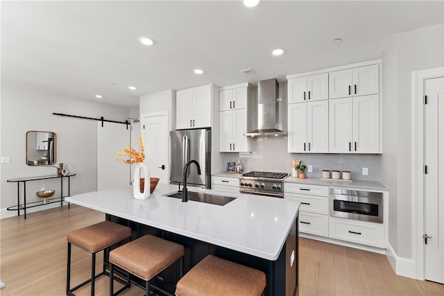 kitchen with a center island with sink, a barn door, sink, and wall chimney exhaust hood