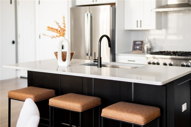 kitchen with white cabinets, stainless steel fridge, a kitchen bar, and exhaust hood