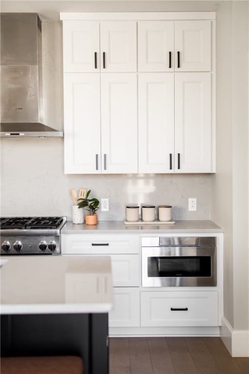 kitchen with white cabinetry, stainless steel appliances, wall chimney exhaust hood, and dark hardwood / wood-style flooring