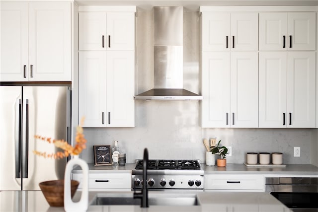 kitchen with wall chimney range hood, appliances with stainless steel finishes, decorative backsplash, and white cabinetry