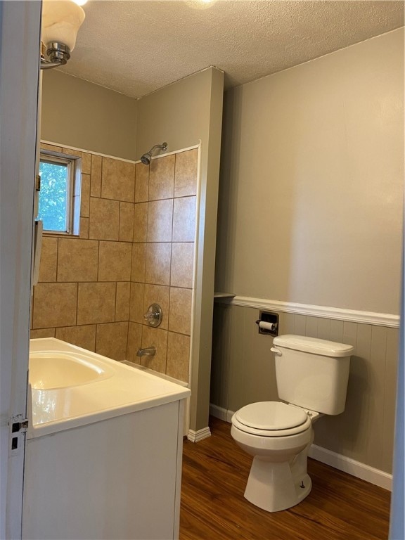 bathroom featuring vanity, wood-type flooring, a textured ceiling, a tile shower, and toilet