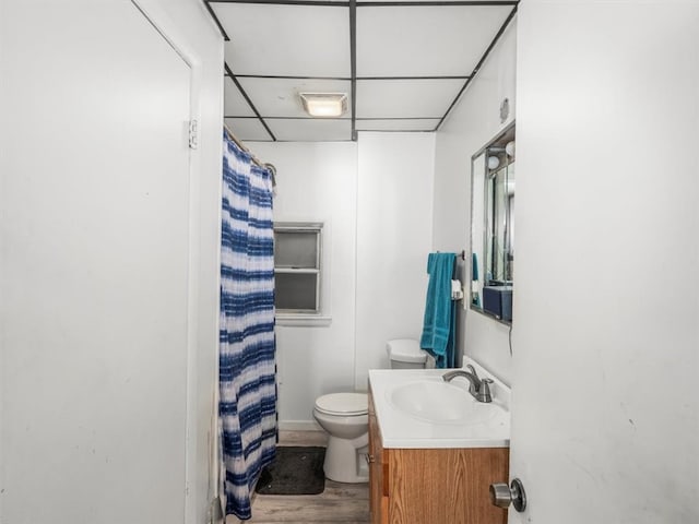 bathroom with walk in shower, toilet, a paneled ceiling, wood-type flooring, and vanity