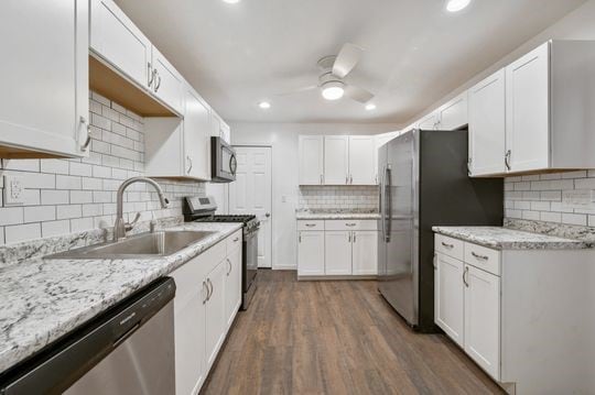 kitchen with light stone countertops, appliances with stainless steel finishes, white cabinetry, dark hardwood / wood-style flooring, and sink